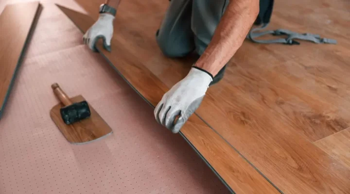 Professional contractor installing luxury vinyl plank flooring over an underlayment during a residential flooring renovation.