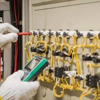 Electrician testing an electrical control panel with a digital multimeter during electrical diagnostics and maintenance