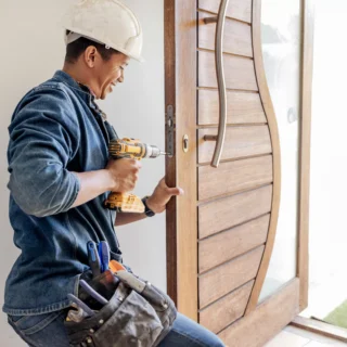 Handyman installing a front entry door with a power drill during residential door replacement service