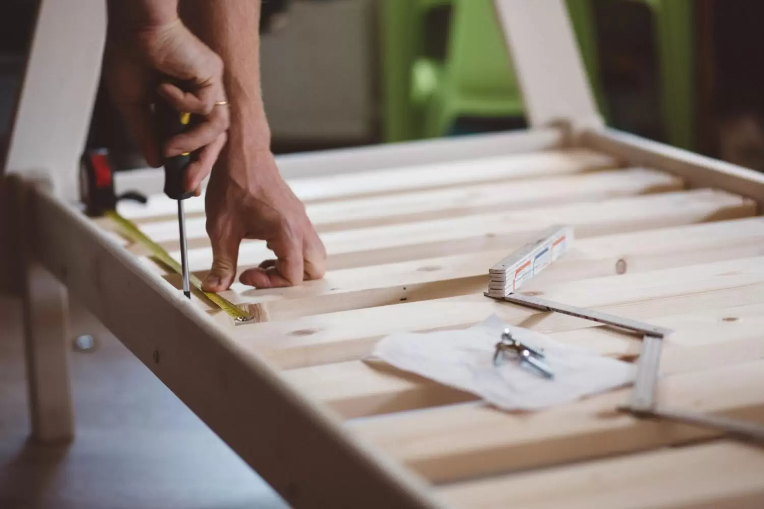 Close-up of a handyman assembling wooden furniture with a screwdriver and measuring tape during home installation