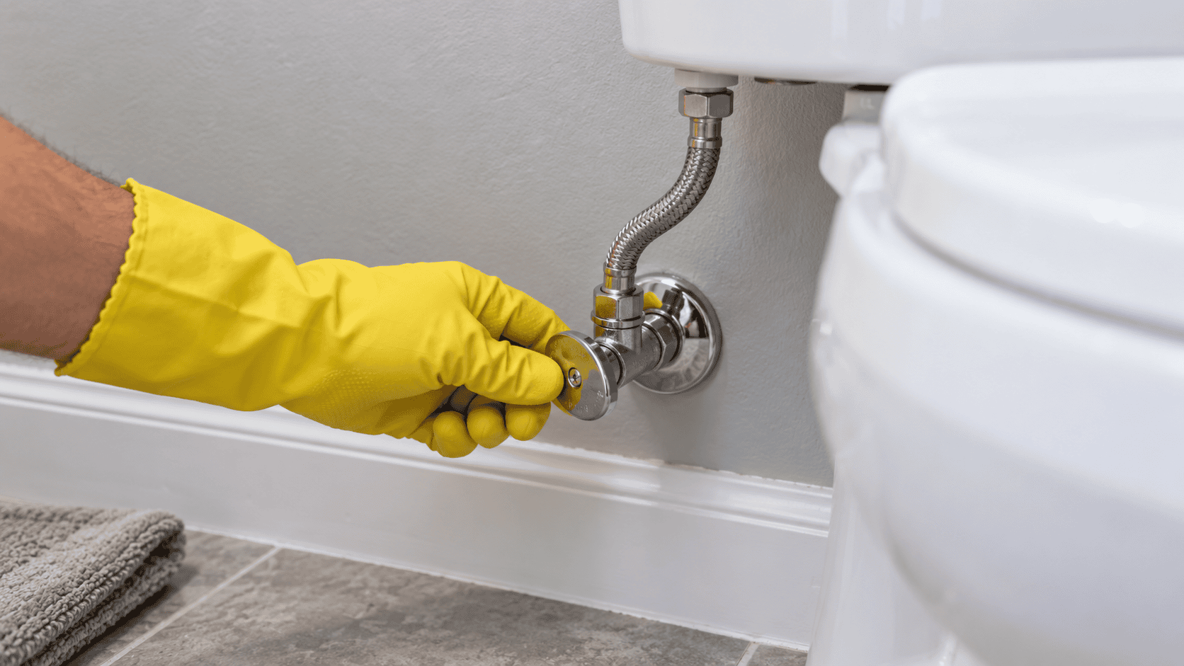 Hand turning the shutoff valve behind a toilet to stop it overflowing